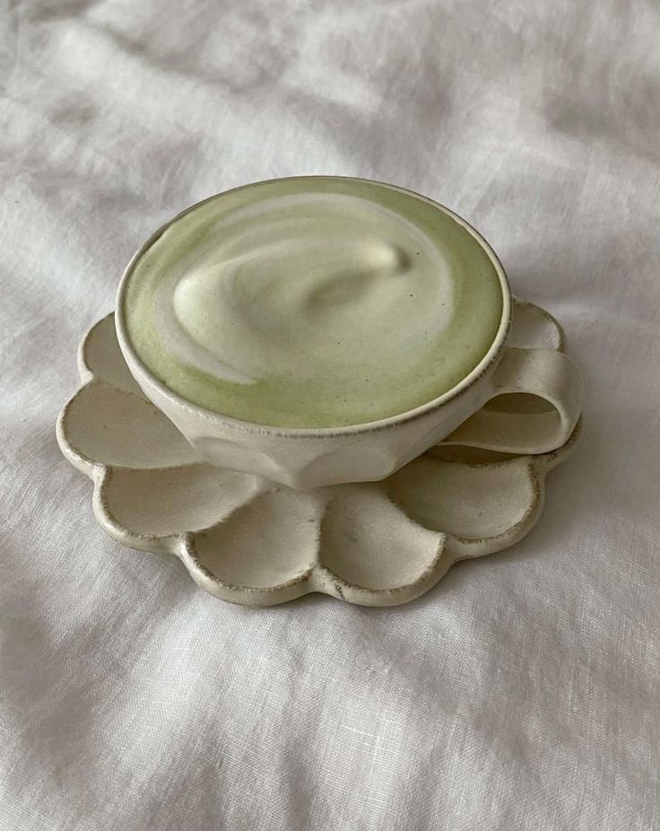 a white bowl sitting on top of a white cloth covered table next to a cup