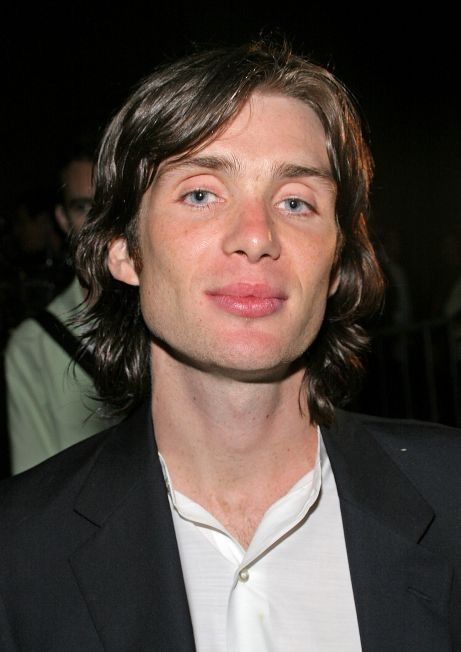 a man with long hair wearing a black suit and white shirt looking at the camera