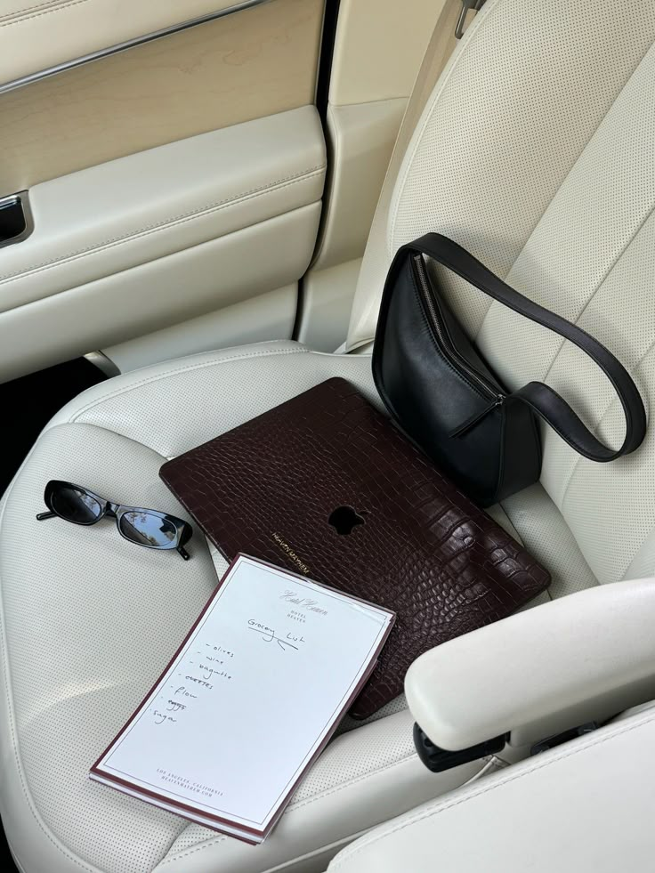 an open laptop computer sitting on top of a white car seat next to a purse