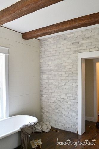 an empty bathroom with exposed beams and white brick walls, including a claw foot bathtub