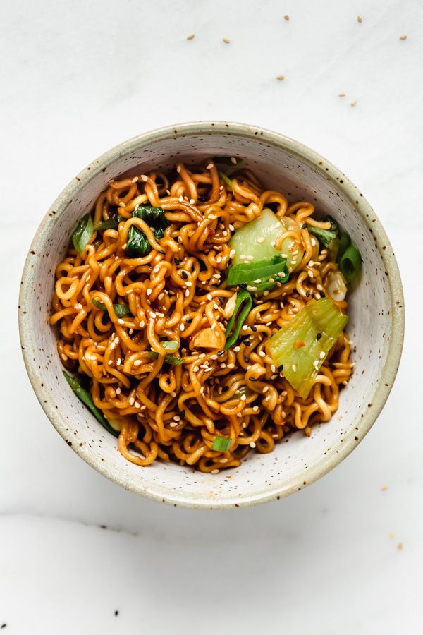 a bowl filled with noodles and vegetables on top of a white countertop next to chopsticks