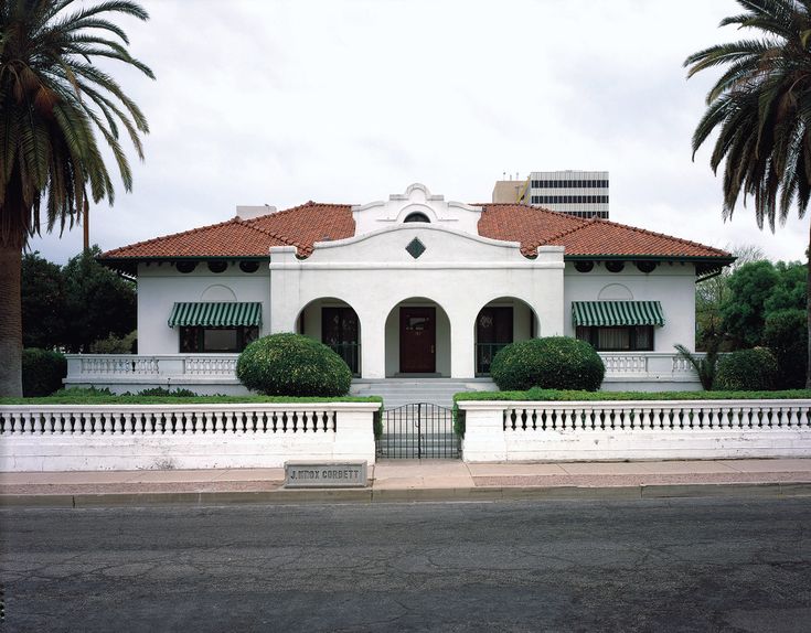 a large white house with palm trees in front of it and a fence around it