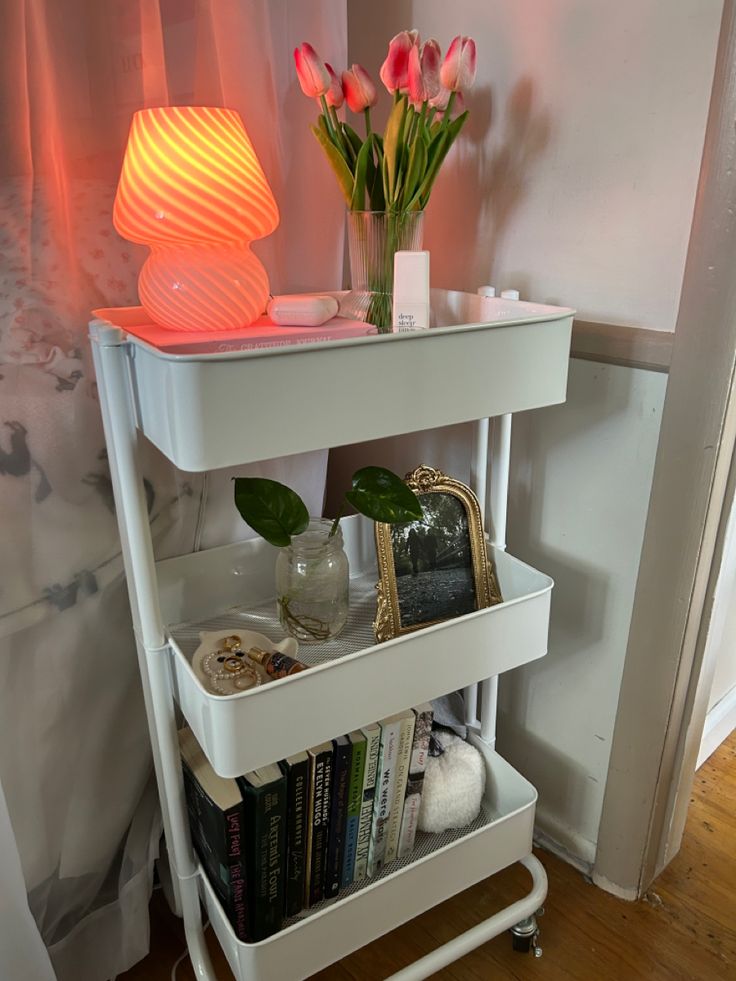 a white shelf with flowers and books on it in front of a light that is turned on