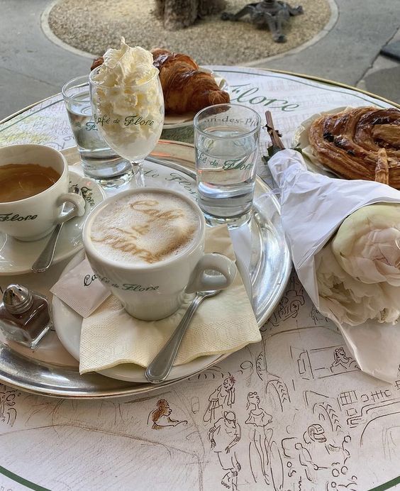 two cups of cappuccino on a table with croissants and pastries