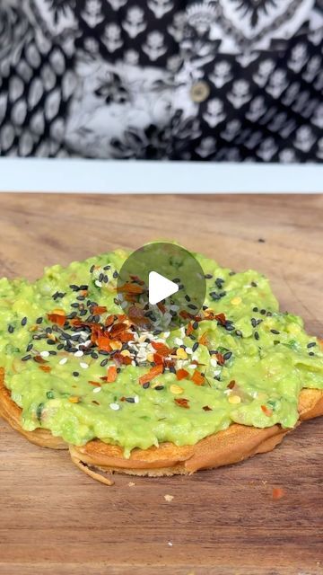 a pizza topped with guacamole and sprinkles on a wooden cutting board