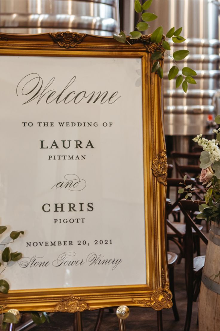 a wedding welcome sign with flowers and greenery in front of a barrel filled with wine