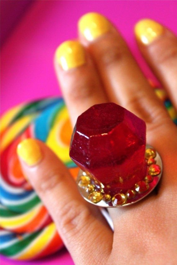 a woman's hand with yellow and red nail polish holding a ring that has a diamond on it