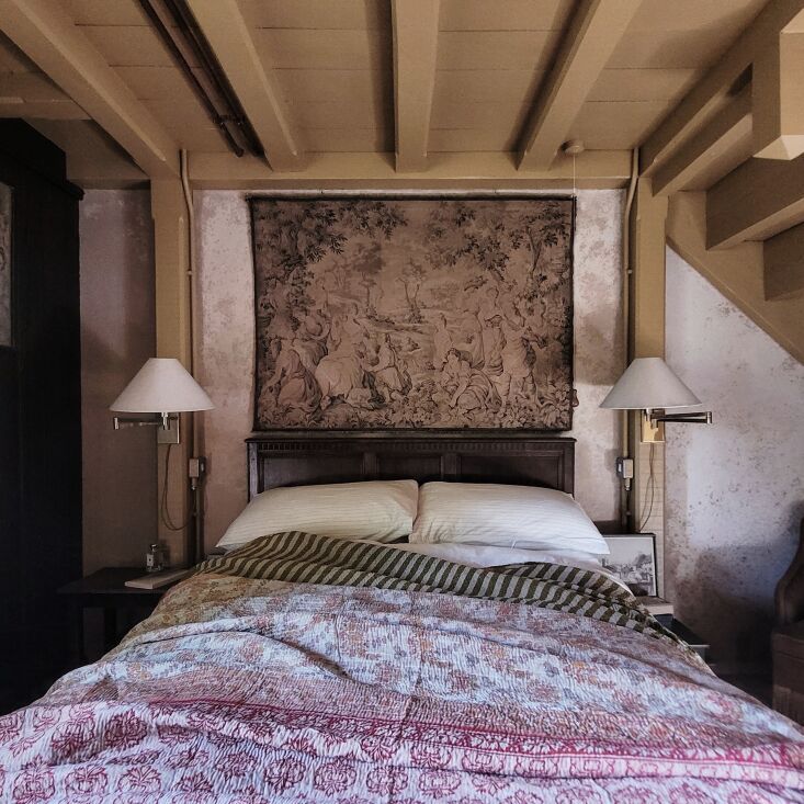 a bed sitting under two lamps on top of a wooden floor next to a wall