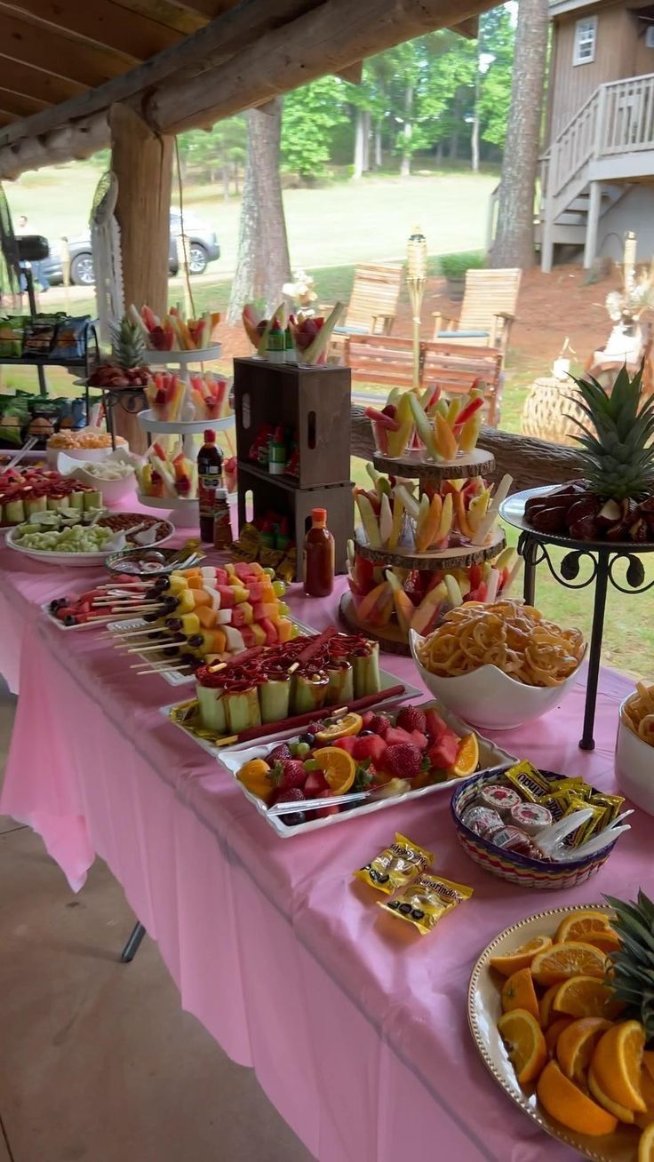 a table filled with lots of food on top of a pink table cloth covered table