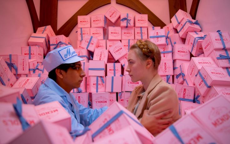 a man and woman sitting in front of stacks of pink boxes with blue writing on them