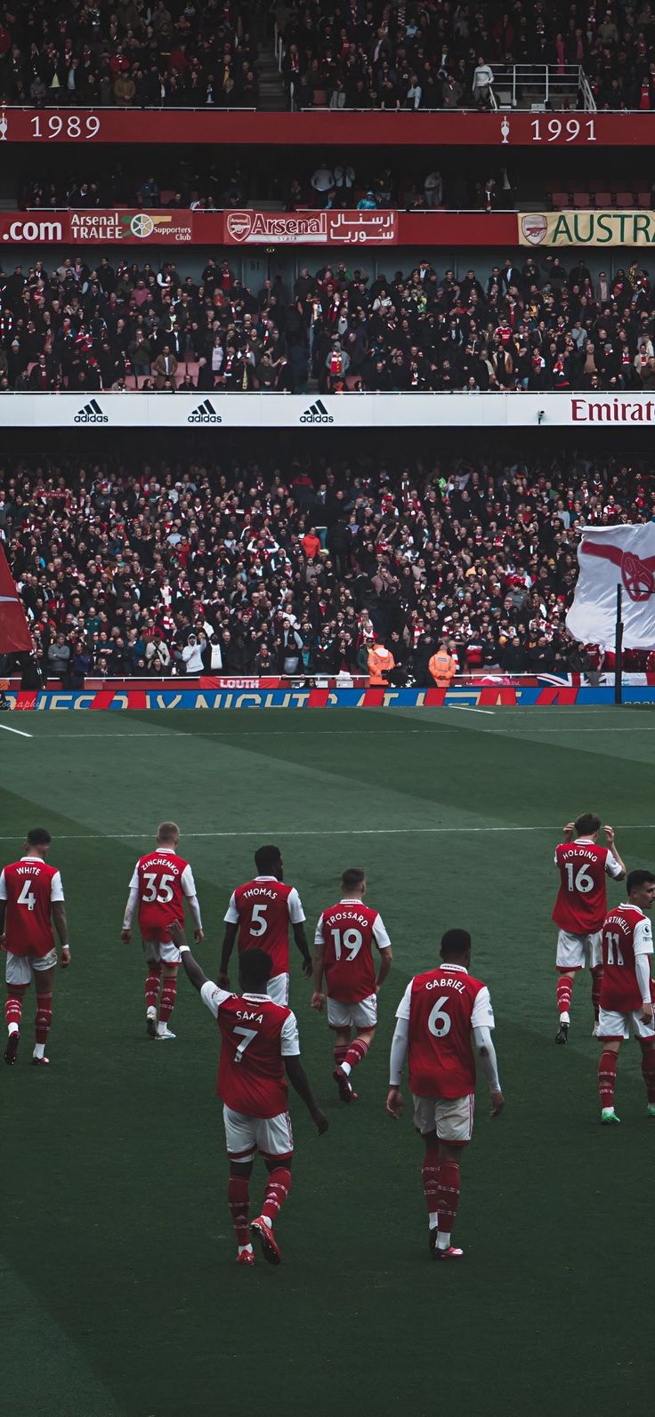 a group of soccer players walking across a field in front of an audience at a stadium