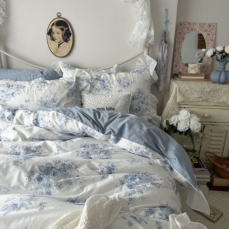 a bed with blue and white comforters in a bedroom next to a dresser filled with flowers