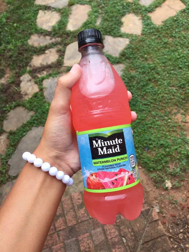 a hand holding a bottle of water with fruit on the top and green grass in the background