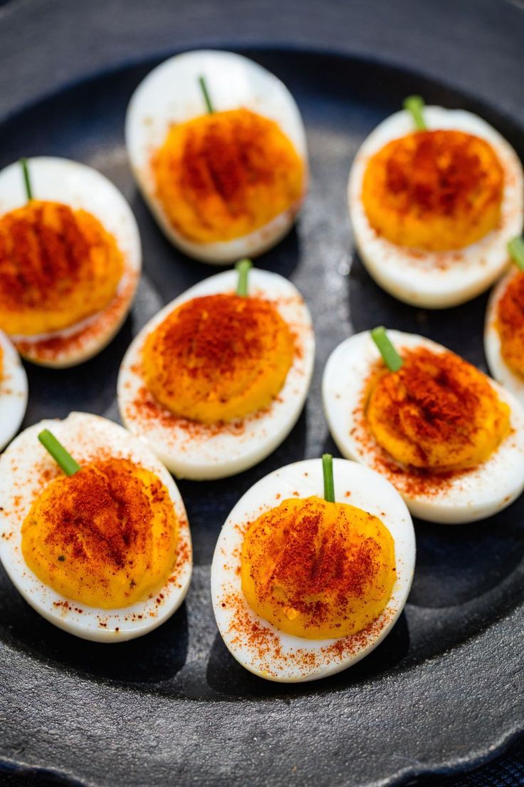 deviled eggs with red chili on top are arranged in a black plate, ready to be eaten