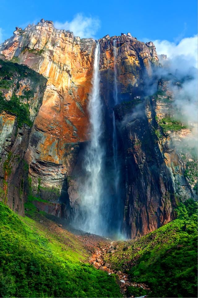 a large waterfall in the middle of a lush green field next to a tall mountain