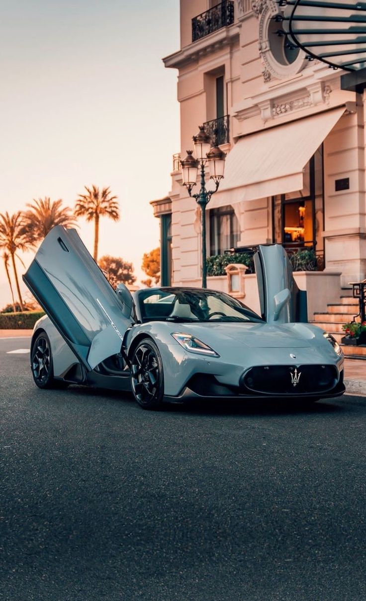 a silver sports car parked in front of a building with its doors open on the street