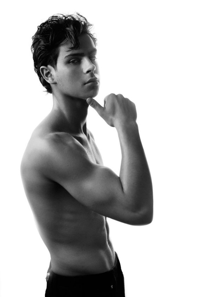 a shirtless young man poses for a black and white photo with his hand on his chin