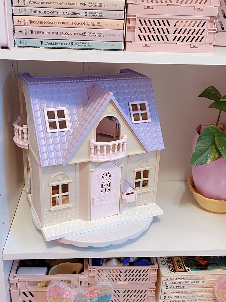 a doll house sitting on top of a white shelf next to other toys and books