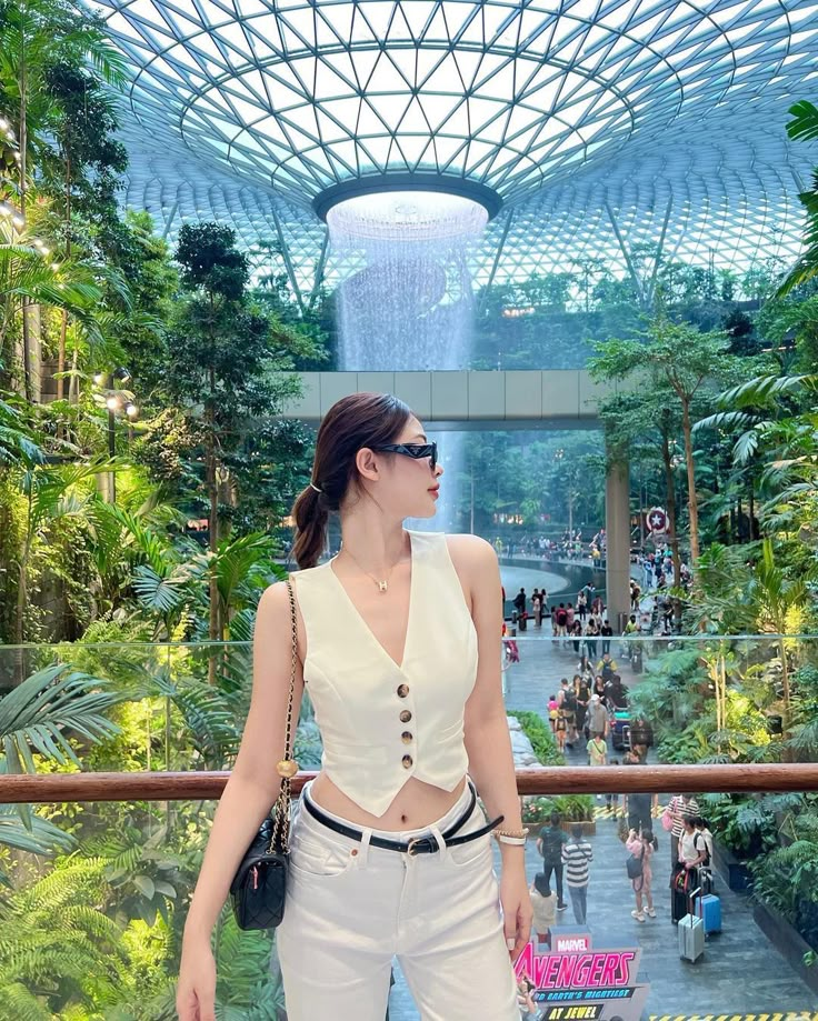 a woman standing in front of a waterfall wearing white pants and a cropped top