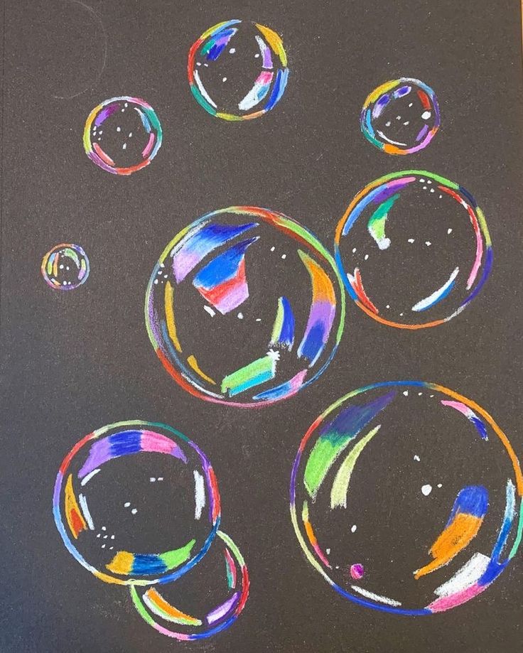 an image of soap bubbles drawn with colored pencils on black paper in front of a wooden table