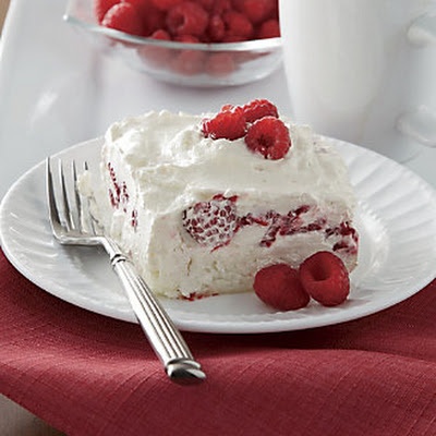 a piece of cake with white frosting and raspberries on the plate next to it