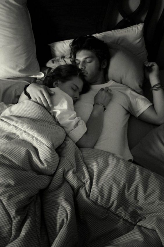 black and white photograph of two people sleeping in bed with pillows on each side of them