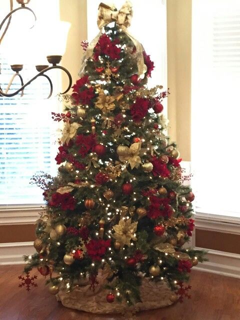 a decorated christmas tree with red and gold ornaments in a living room area next to a chandelier