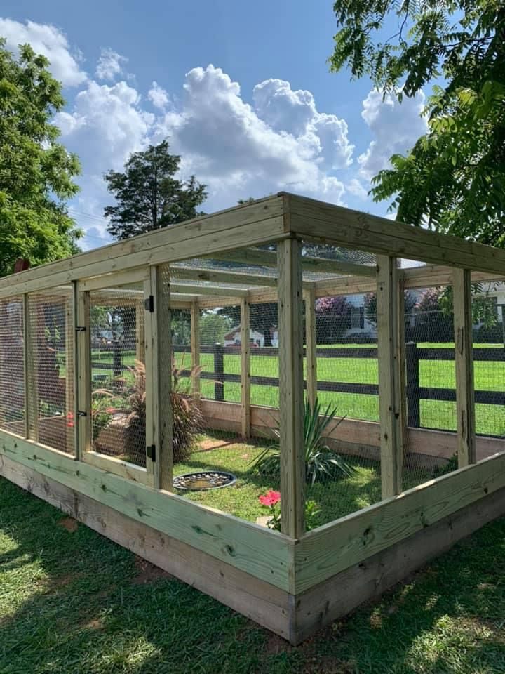 a wooden structure with plants in it on the grass near some trees and fenced in area