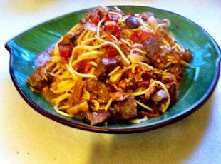 a green plate topped with pasta and meat on top of a white table next to a fork