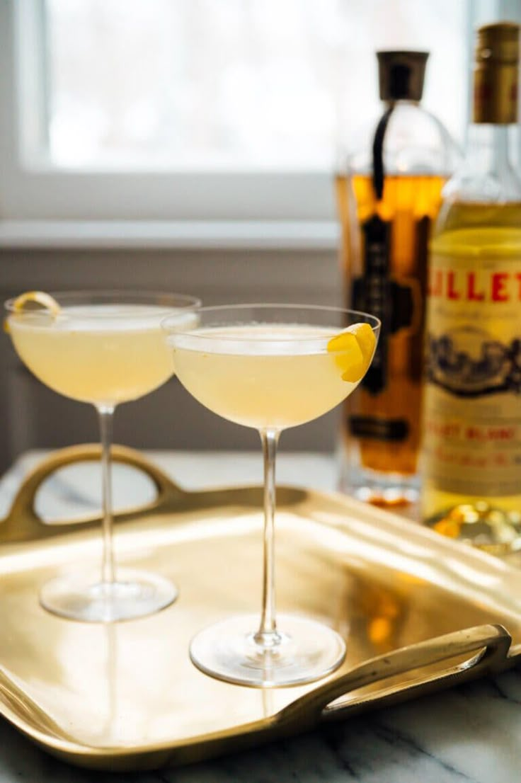 two martinis on a tray with bottles in the background