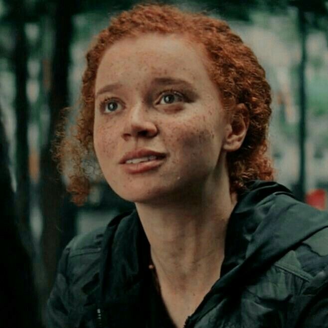 a woman with freckles on her face looks into the distance while standing outside