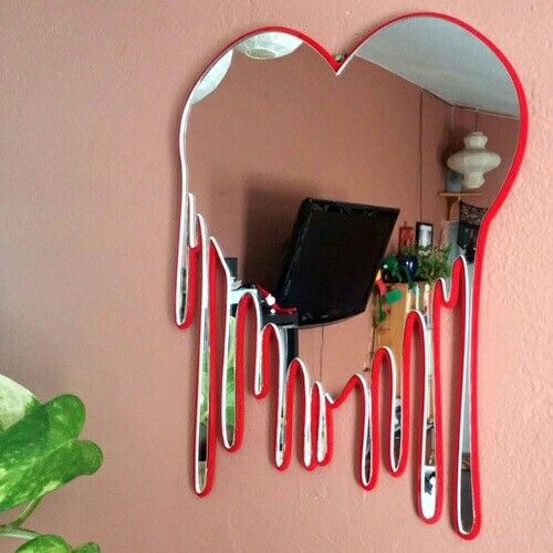 a heart shaped mirror hanging on the side of a pink wall next to a plant