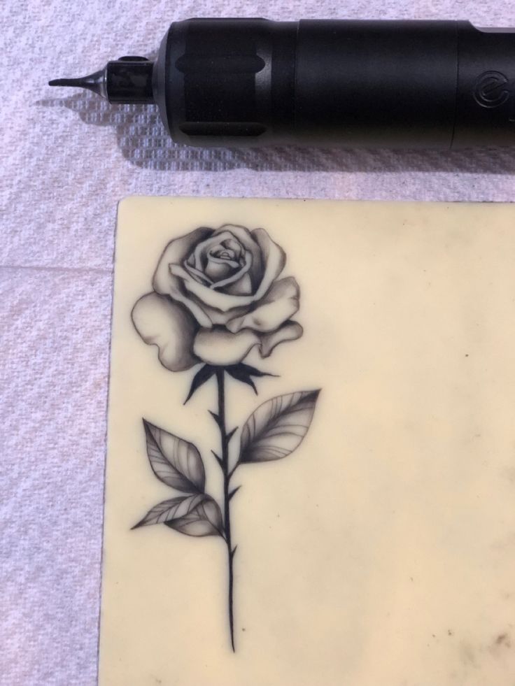 a rose tattoo on the side of a piece of paper next to an ink pen