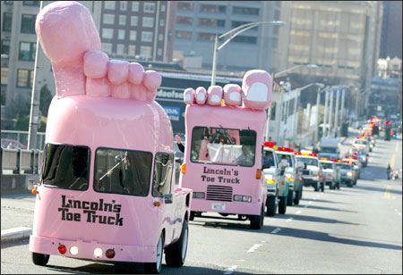 two pink vehicles driving down the road with giant hands on their backs and feet sticking out