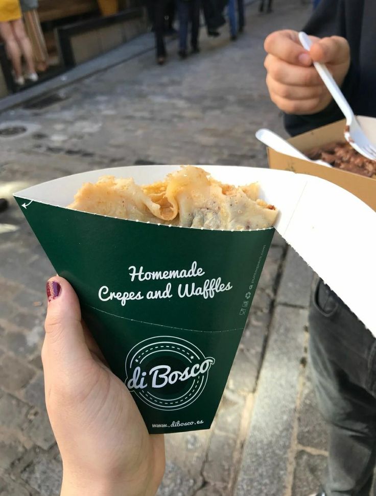 a person holding up a box of food on the street with other people in the background