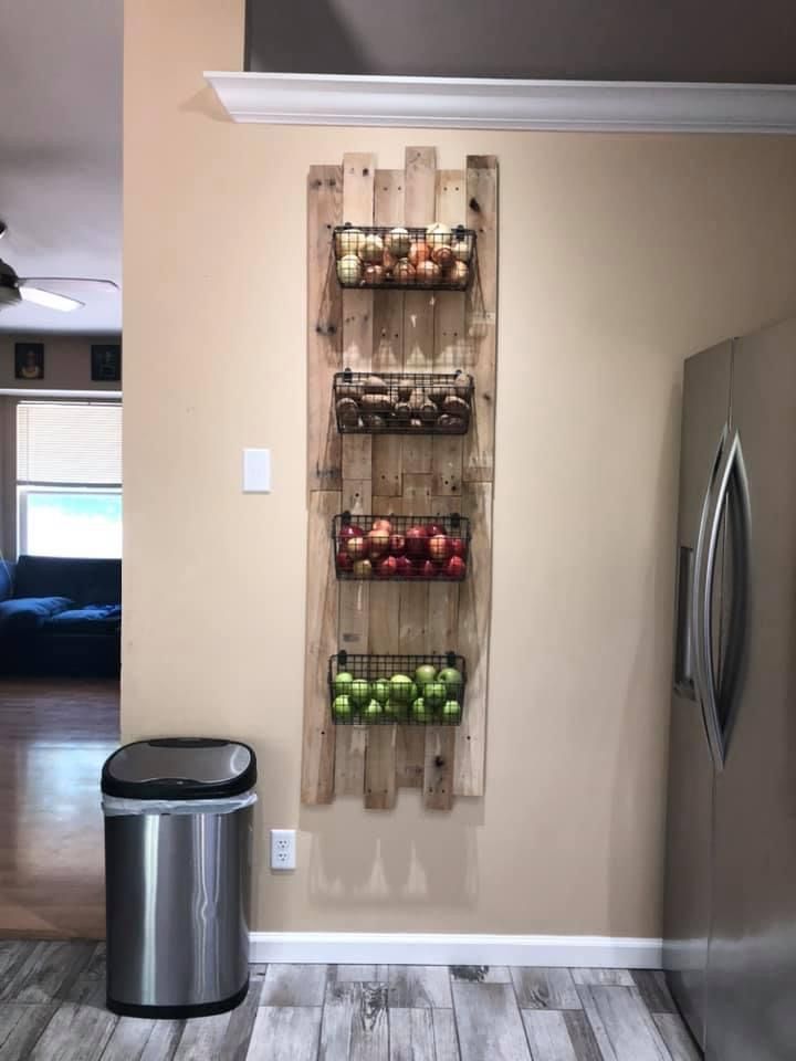 a wooden rack with apples and other fruit in it on the wall next to a stainless steel trash can