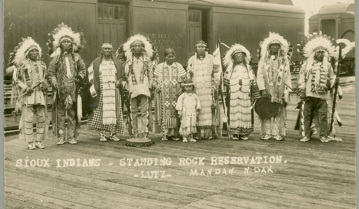 an old black and white photo of native american indians standing in front of a train