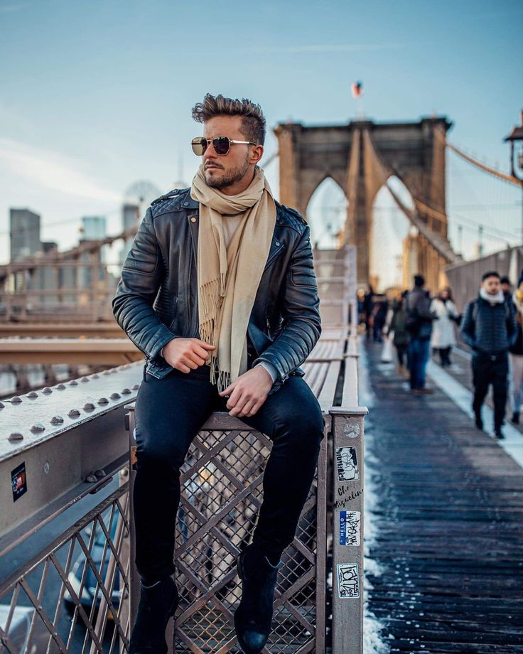 a man sitting on the edge of a bridge wearing sunglasses and a scarf over his head