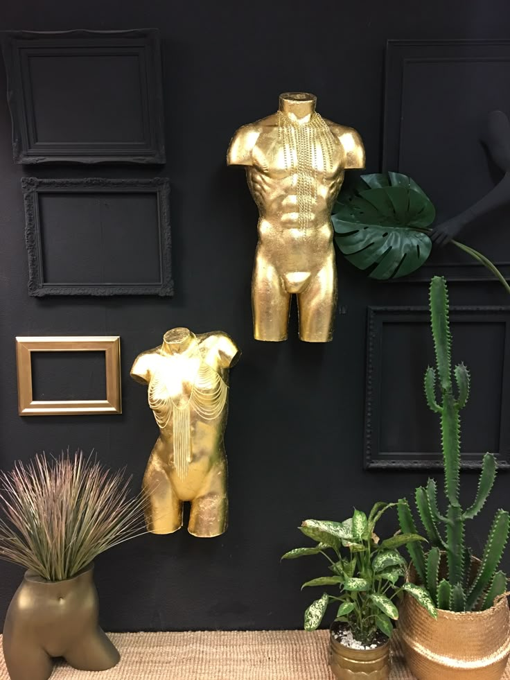 two gold statues are on display next to plants and other decorative items in front of a black wall