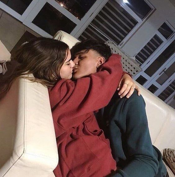 two people sitting on a couch with their arms around each other and one person kissing the other