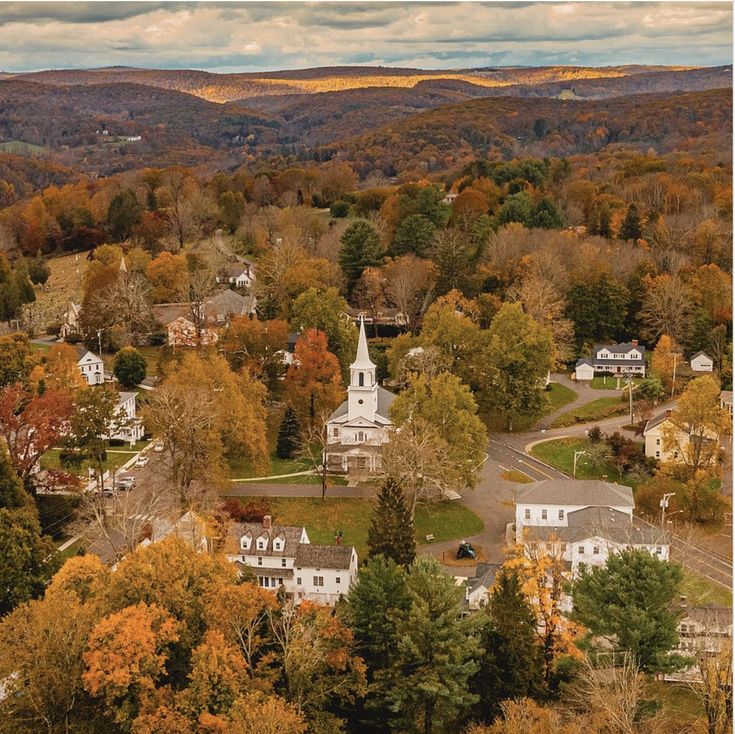 an aerial view of a small town surrounded by trees and mountains in the fall season