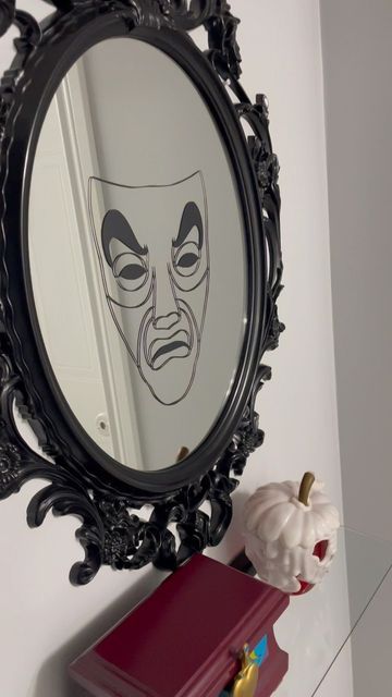 a mirror with a face drawn on it next to a small red box and vase