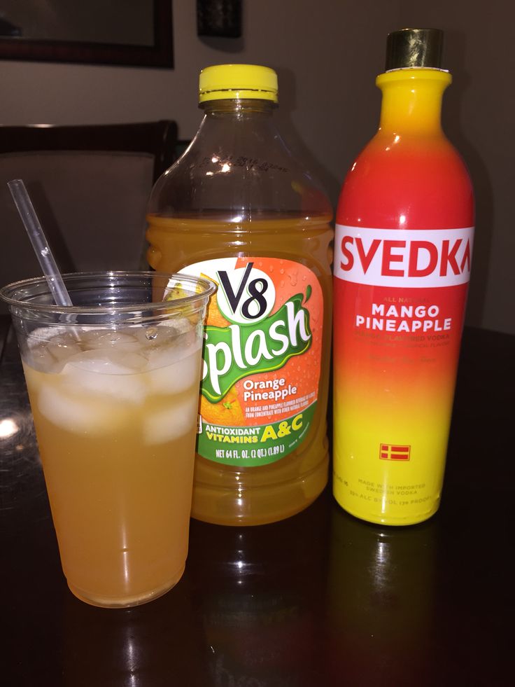 two bottles and a glass sitting on a table next to an orange drink with a straw in it