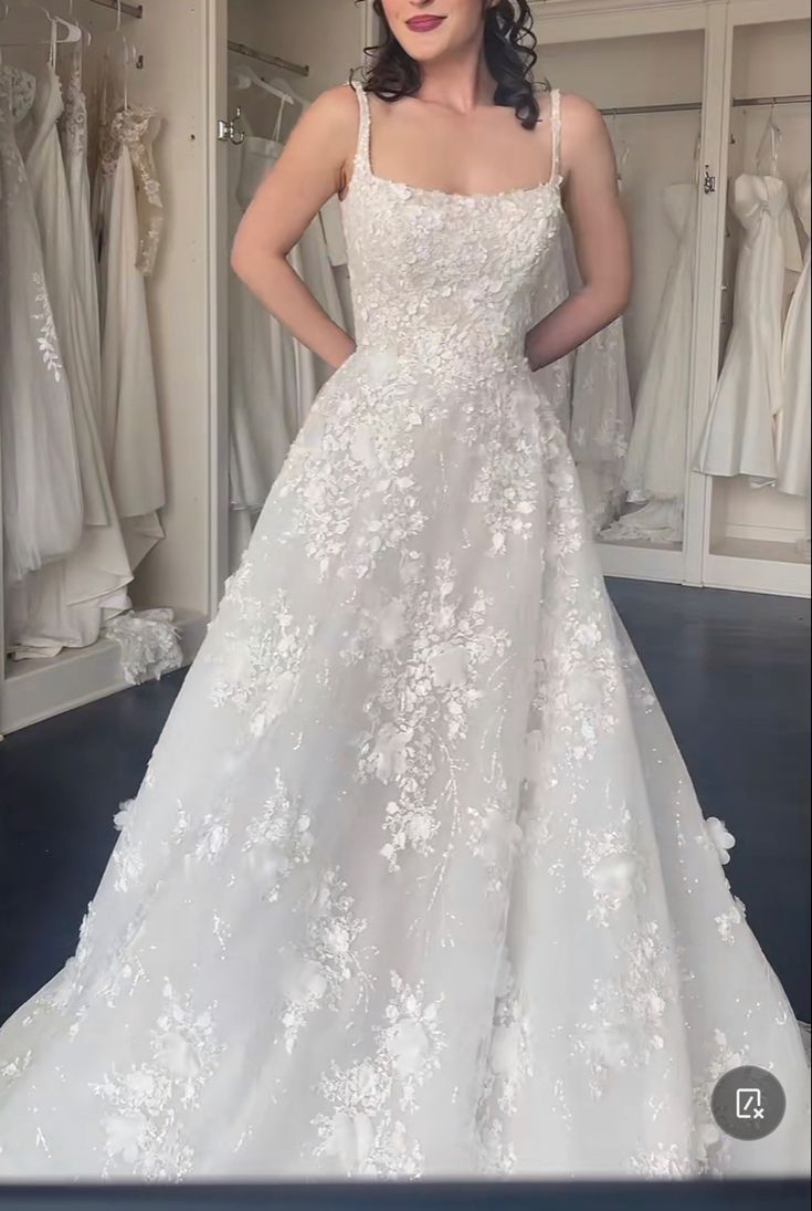 a woman standing in front of a mirror wearing a wedding dress with white flowers on it