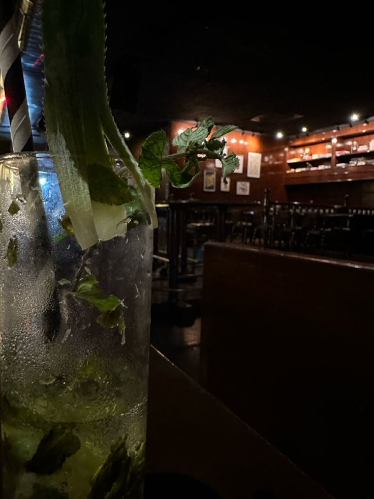 a tall glass filled with ice and green leaves sitting on top of a wooden table