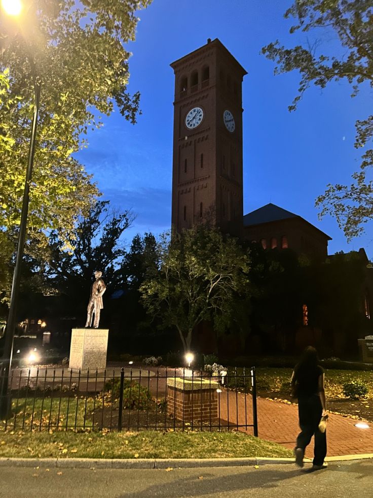 a tall clock tower towering over a lush green park next to a fenced in area