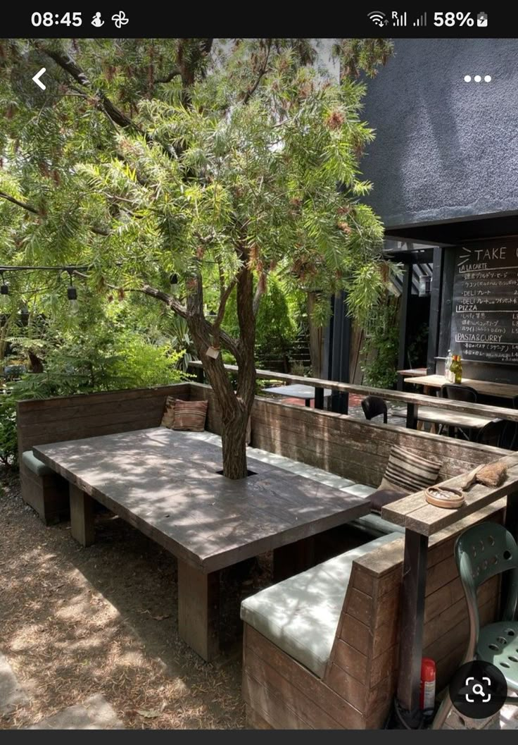 an outdoor table and benches in front of a tree with chalkboard on the wall