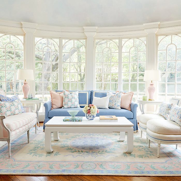 a living room filled with lots of furniture next to two large windows and a rug on the floor