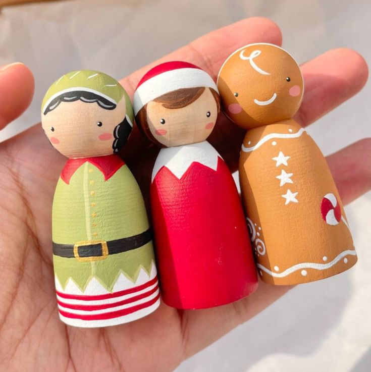 a hand holding three wooden dolls in different colors