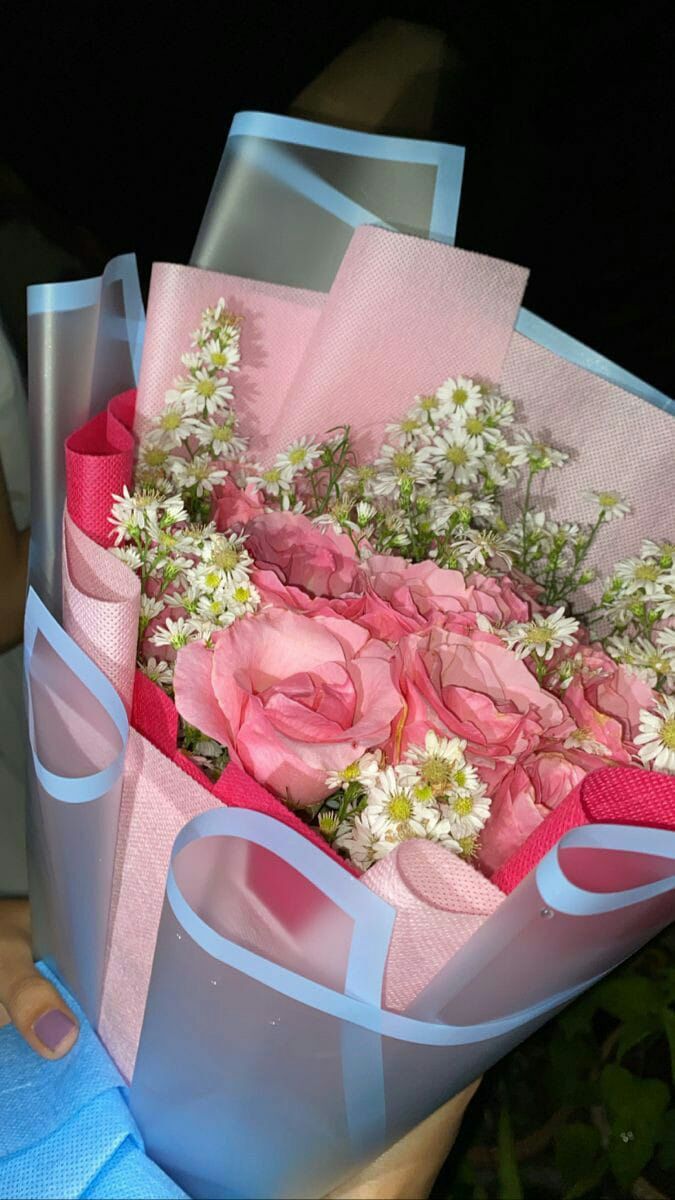 a bouquet of pink roses and white flowers in a blue paper wrapped gift bag with ribbon